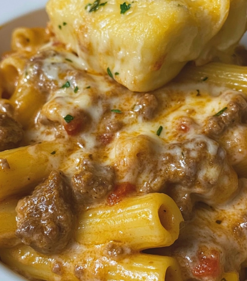 Creamy beef and cheese pasta served in a bowl with a garlic knot, showcasing a rich, cheesy sauce.