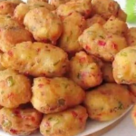 Vegetable fritters in a bowl with a crispy golden exterior, alongside a mixing bowl of batter with colorful chopped vegetables.