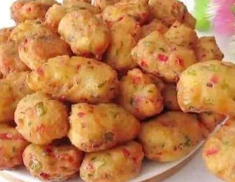 Vegetable fritters in a bowl with a crispy golden exterior, alongside a mixing bowl of batter with colorful chopped vegetables.