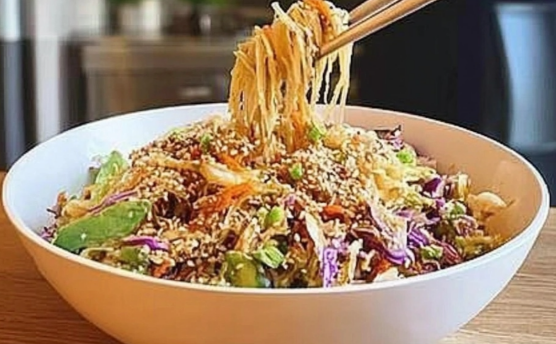 Crunchy Asian slaw with colorful shredded vegetables and sesame dressing being poured over the top.