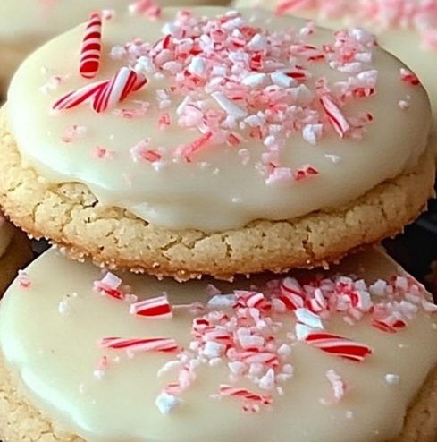 Peppermint Cheesecake Cookies topped with creamy frosting, crushed peppermint candies, and pink drizzle.