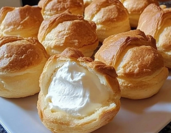 Golden cream puffs with a fluffy whipped filling, arranged on a white plate.